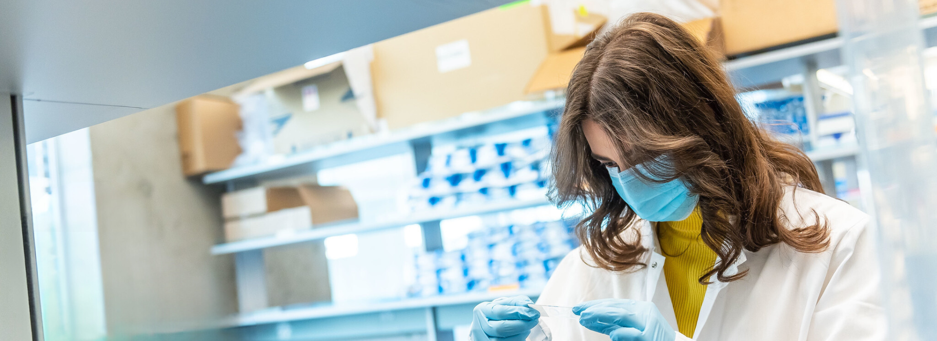 A brunette woman in a lab looking at a sample in lab gear