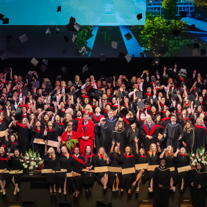UBC Faculty of Medicine's MD Undergraduate Program Class of 2024 celebrating and tossing their hats on stage with faculty members.
