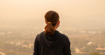 A woman wearing a face mask looking over her community covered in a thick haze of wildfire smoke.
