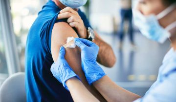 A close-up of a healthcare provider applying a band aid on a patient’s upper arm after vaccination.