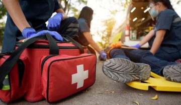 Three paramedics assist an injured person on a stretcher, first aid kit visible.